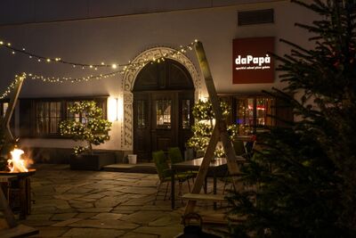 Das Restaurant 7132 daPapa in Vals (7132, Kanton Graubuenden) zeigt einen festlich beleuchteten Eingang mit Lichterketten, Feuerstelle und gemuetlicher Atmosphaere.