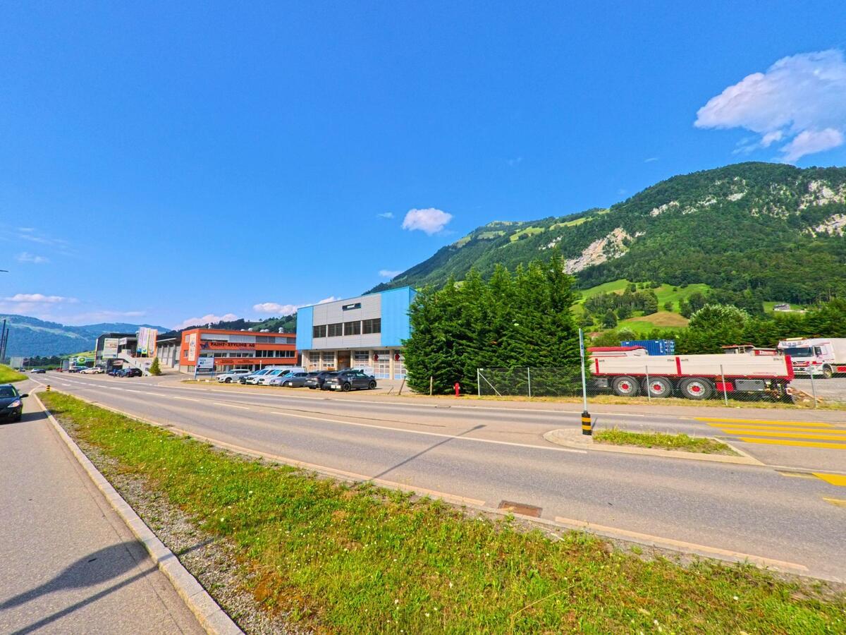 Gewerbebauten mit grossen Hallen praegen das Bild entlang der Hauptstrasse in Dallenwil (6382, Kanton Nidwalden), vor einer Kulisse aus gruener Berglandschaft.