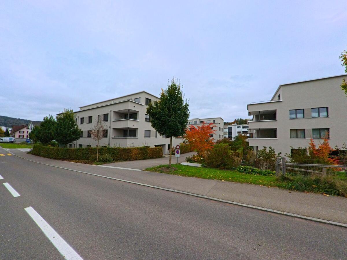 Mehrere moderne Mehrfamilienhäuser mit Balkonen liegen entlang einer ruhigen Quartierstrasse mit Grünflächen in Aadorf (8355, Kanton Thurgau).