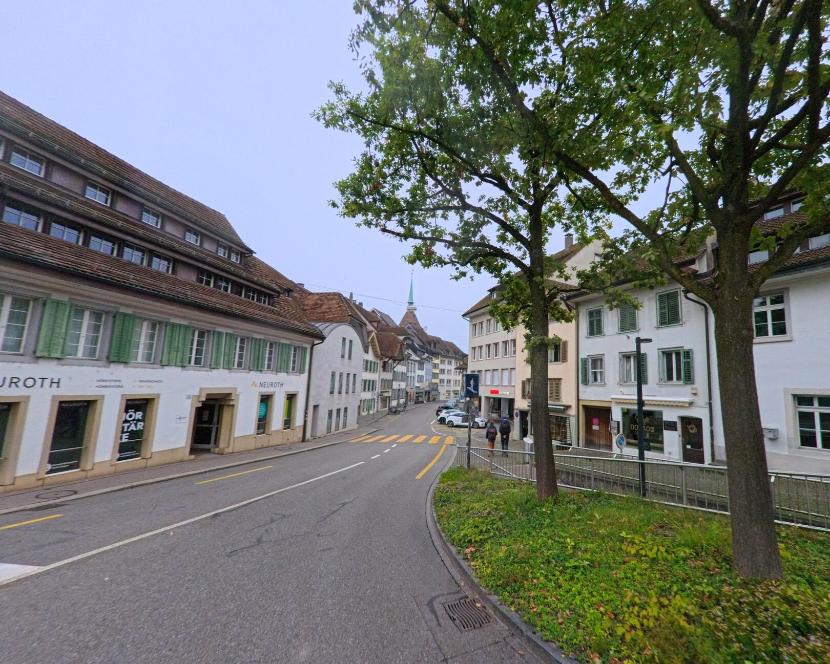 In Aarau (5000, Kanton Aargau) säumen farbenfrohe historische Häuser den zentralen Platz mit Kopfsteinpflaster, im Vordergrund steht ein Brunnen mit steinerner Säule.