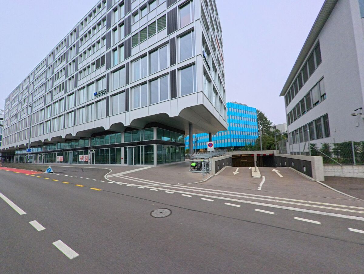In Aarau (5001, Kanton Aargau) stehen moderne Bürogebäude mit grossen Glasfassaden entlang einer breiten Strasse, daneben führt eine Rampe zu einer Tiefgarage hinunter.