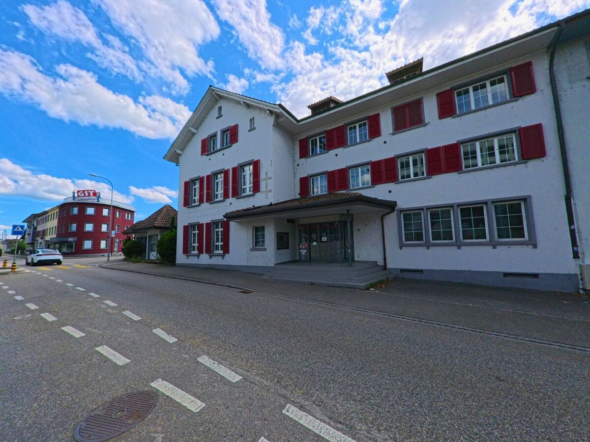 In Aarburg (4663, Kanton Aargau) stehen zwei markante Gebaeude mit roten Fensterlaeden und der Aufschrift „GST“ an einer Kreuzung mit Fussgaengerstreifen und abzweigender Nebenstrasse.