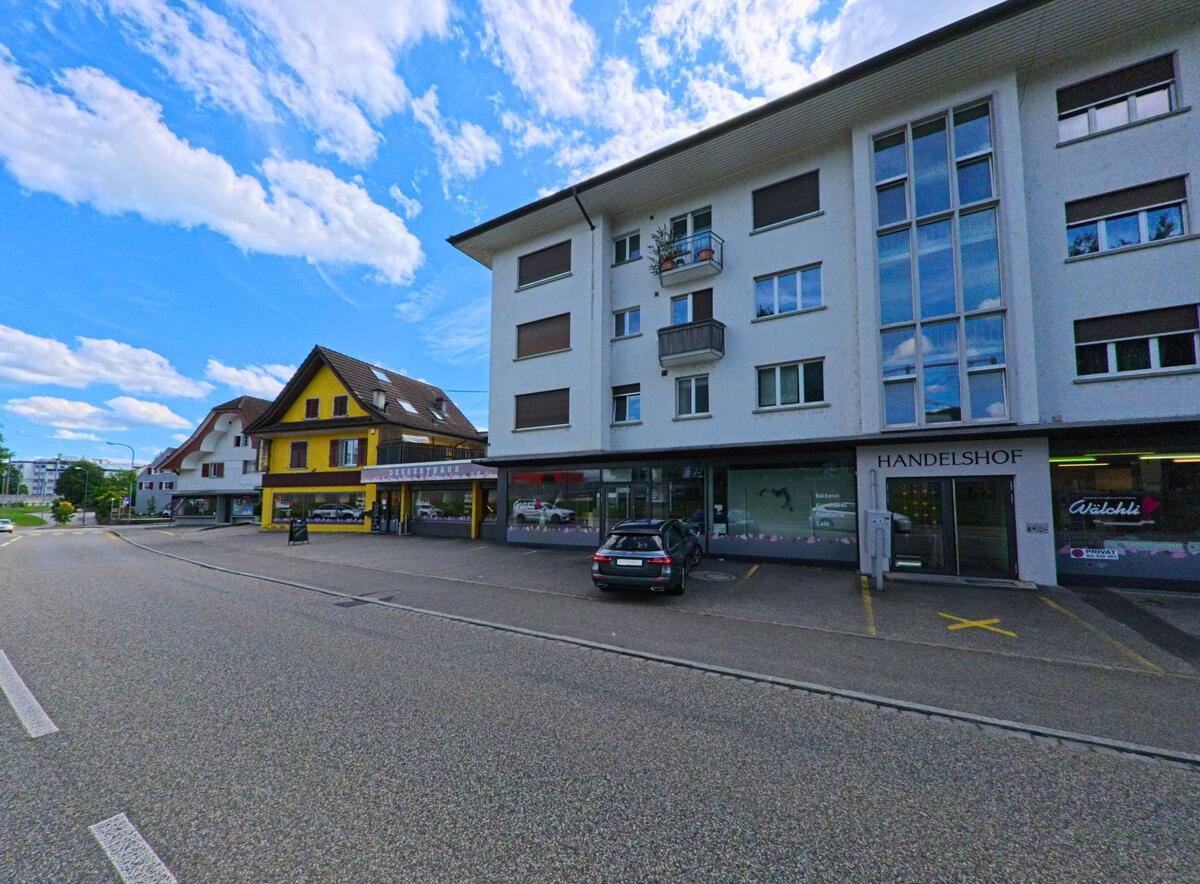 An der Hauptstrasse von Aarburg (4663, Kanton Aargau) reihen sich moderne Wohn- und Geschaeftshaeuser mit verschiedenen Ladengeschaeften, darunter ein auffaellig gelbes Gebaeude mit Baeckerei.