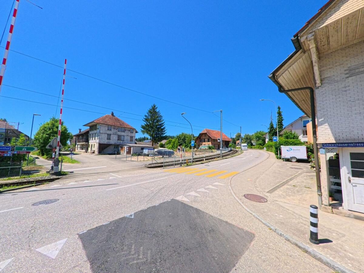 In Aarwangen (4912, Kanton Bern) verlaeuft die Schwarzhäusernstrasse entlang einer Bahnlinie, die von einem unbeschrankten Bahnuebergang mit roten Signalmasten begleitet wird.