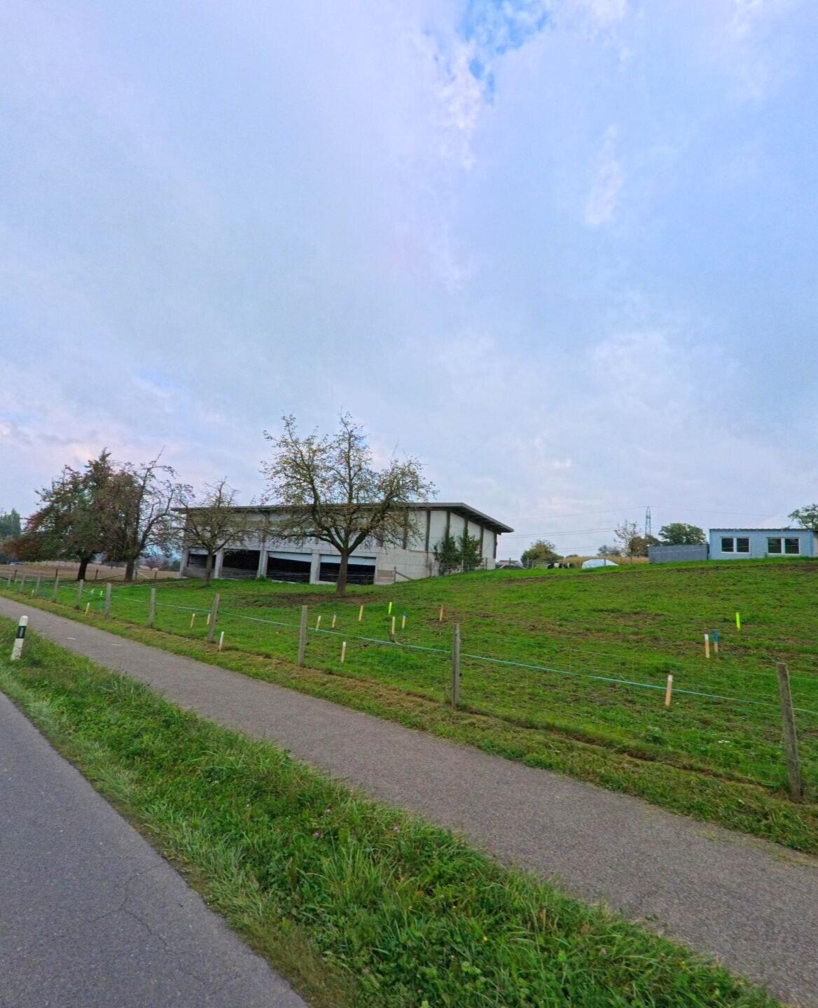 Ein Landwirtschaftsgebäude steht in Abtwil (5646, Kanton Aargau) auf einer leicht ansteigenden Wiese mit eingezäuntem Weg im Vordergrund.