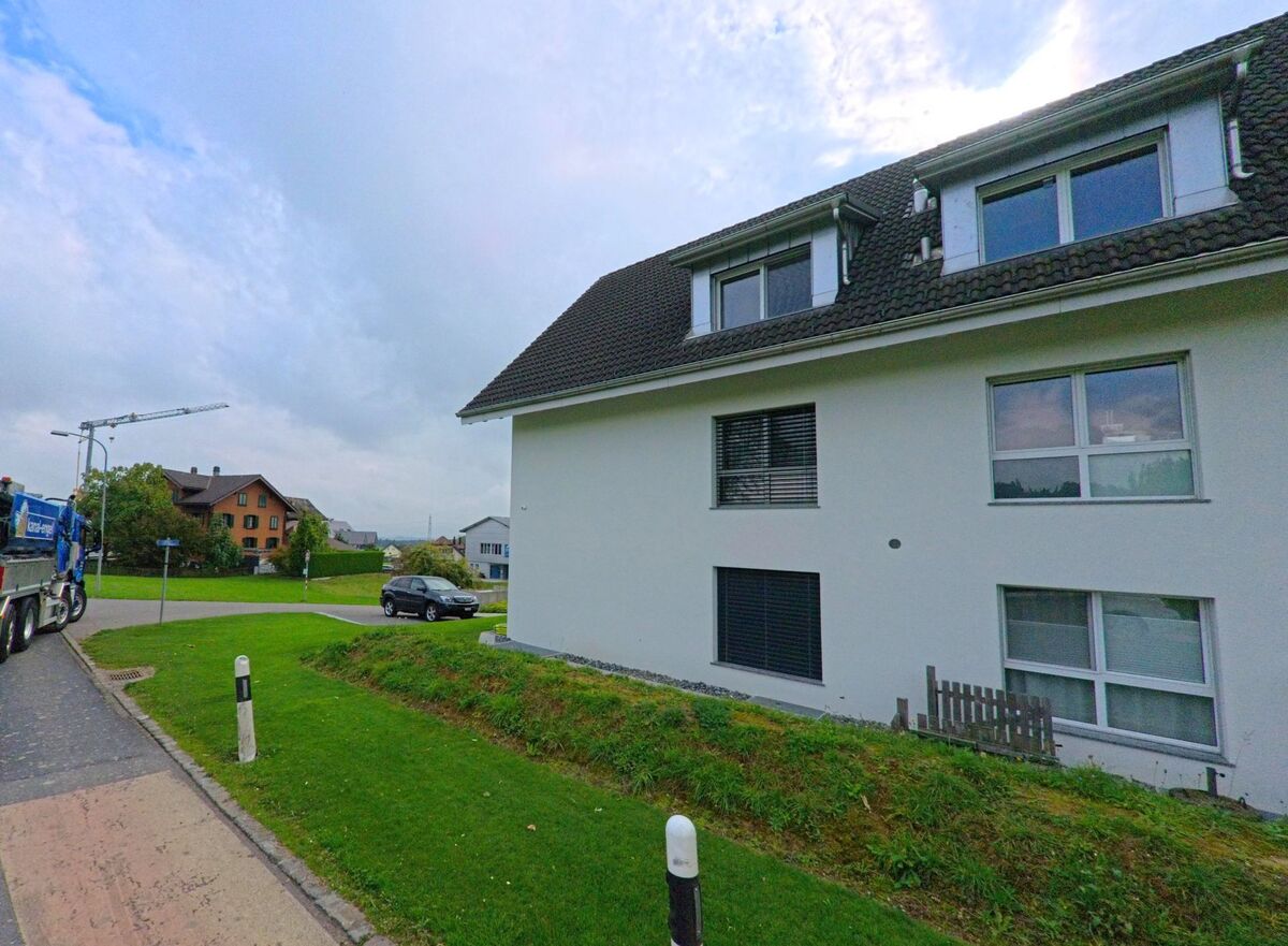 Ein modernes Mehrfamilienhaus in Abtwil (5646, Kanton Aargau) steht an einer Strassenkreuzung mit gepflegtem Rasen und Blick auf weitere Wohnhaeuser.