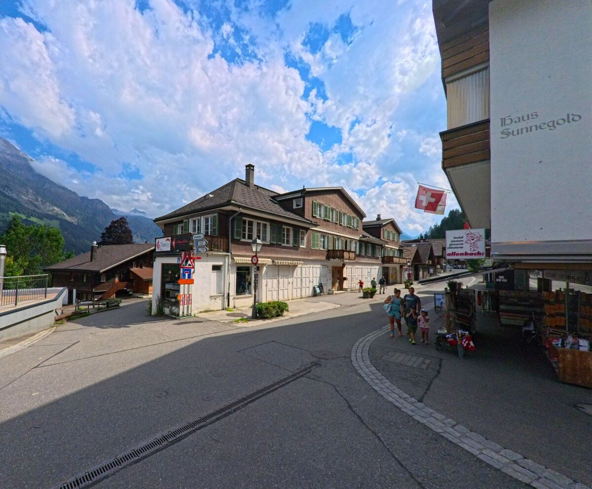 In der Gemeinde Adelboden (3715, Kanton Bern) stehen traditionelle Holzhäuser mit Läden im Erdgeschoss an einer verkehrsberuhigten Kreuzung mit Kopfsteinpflaster.