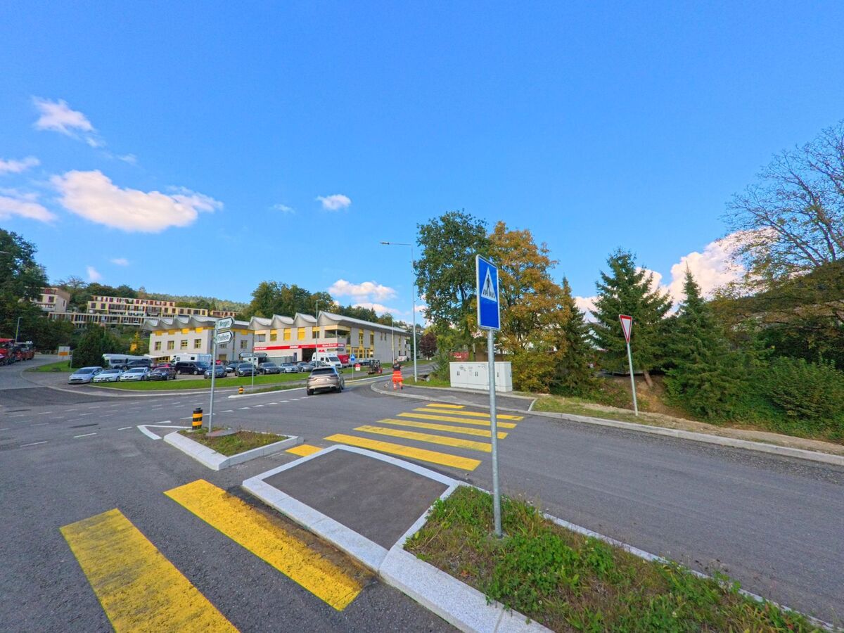 Eine Kreuzung mit Zebrastreifen in Adligenswil (6043, Kanton Luzern) führt zu modernen Gebäuden und einem Garagenbetrieb am Hang.