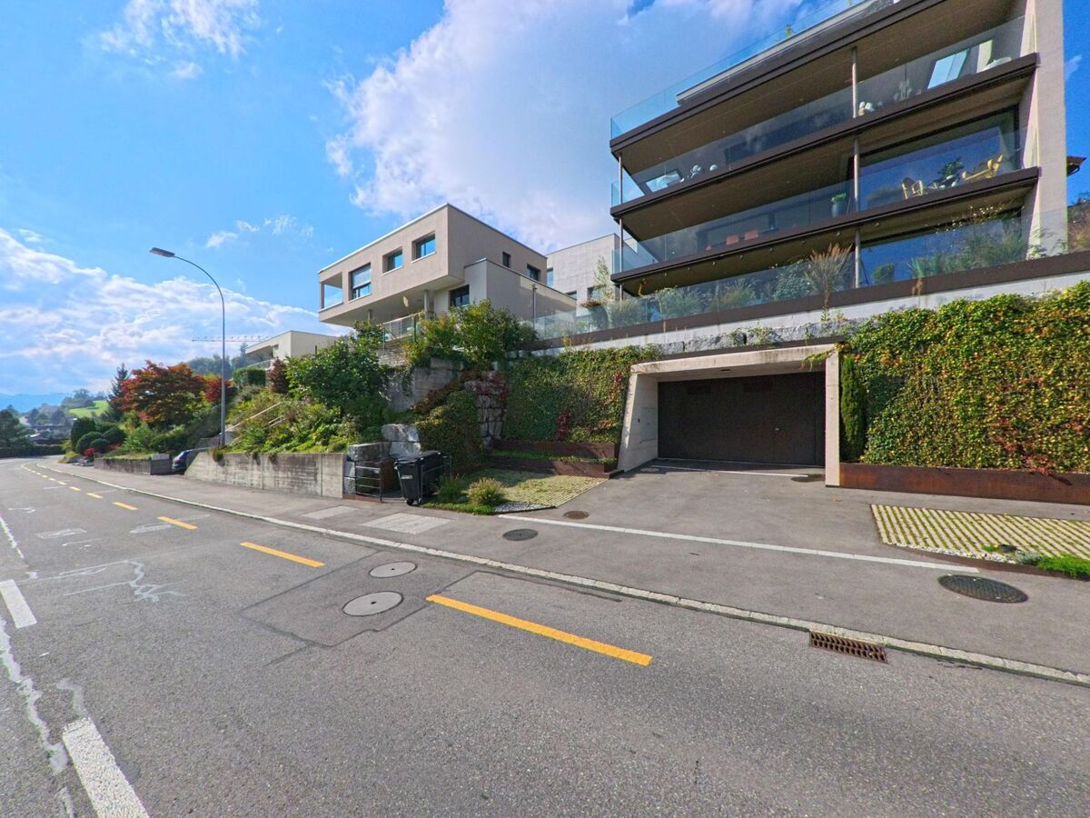 In Adligenswil (6043, Kanton Luzern) stehen moderne Wohnhäuser mit grossen Glasfassaden und gepflegten Gärten an einer ruhigen Strasse.