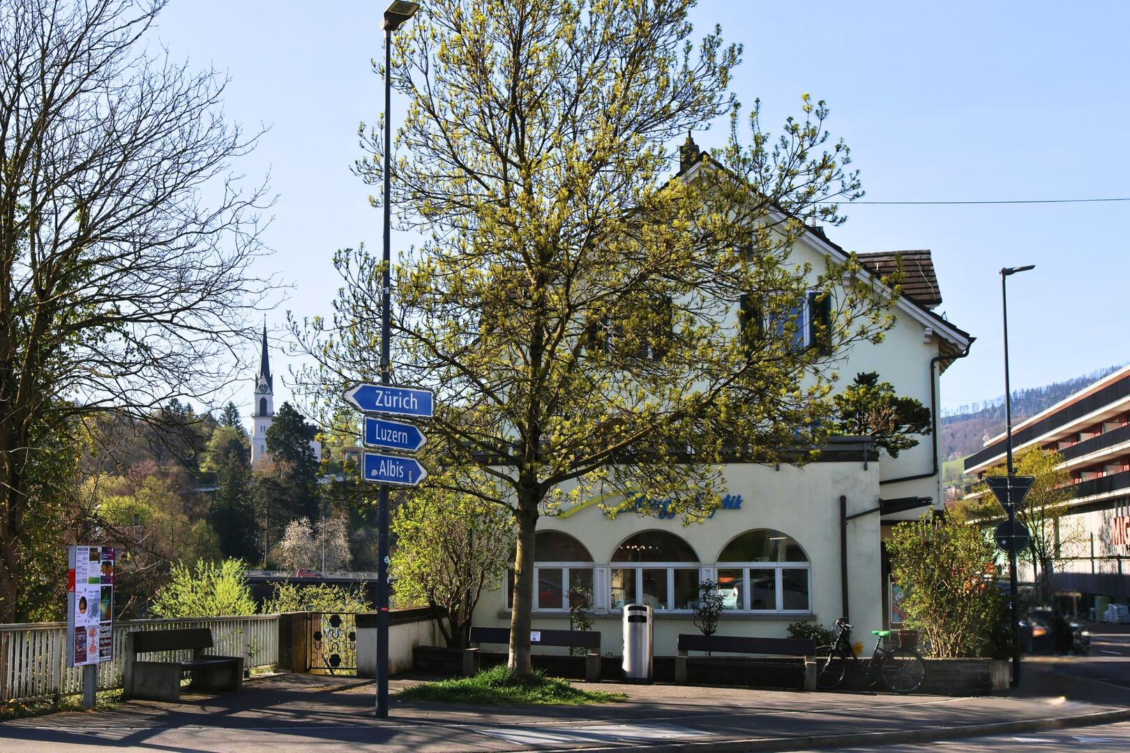 In Adliswil (8134, Kanton Zürich) steht an einer belebten Kreuzung ein Gebäude mit Blick auf Wegweiser nach Zürich, Luzern und Albis.