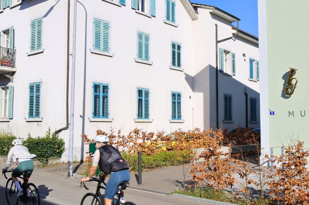 In Adliswil (8134, Kanton Zürich) fährt ein Velofahrer am Musikhaus mit blauer Fensterfassade und Instrumentendekor vorbei.