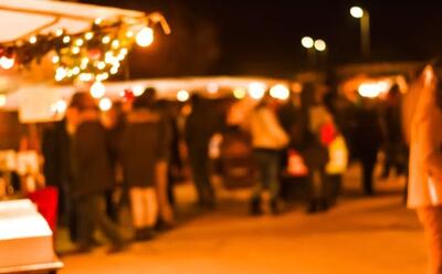 Bei Nacht zeigt das Bild in Treiten (3226, Kanton Bern) einen stimmungsvoll beleuchteten Adventsmaerit mit Marktstaenden und unscharfen Besuchergruppen.
