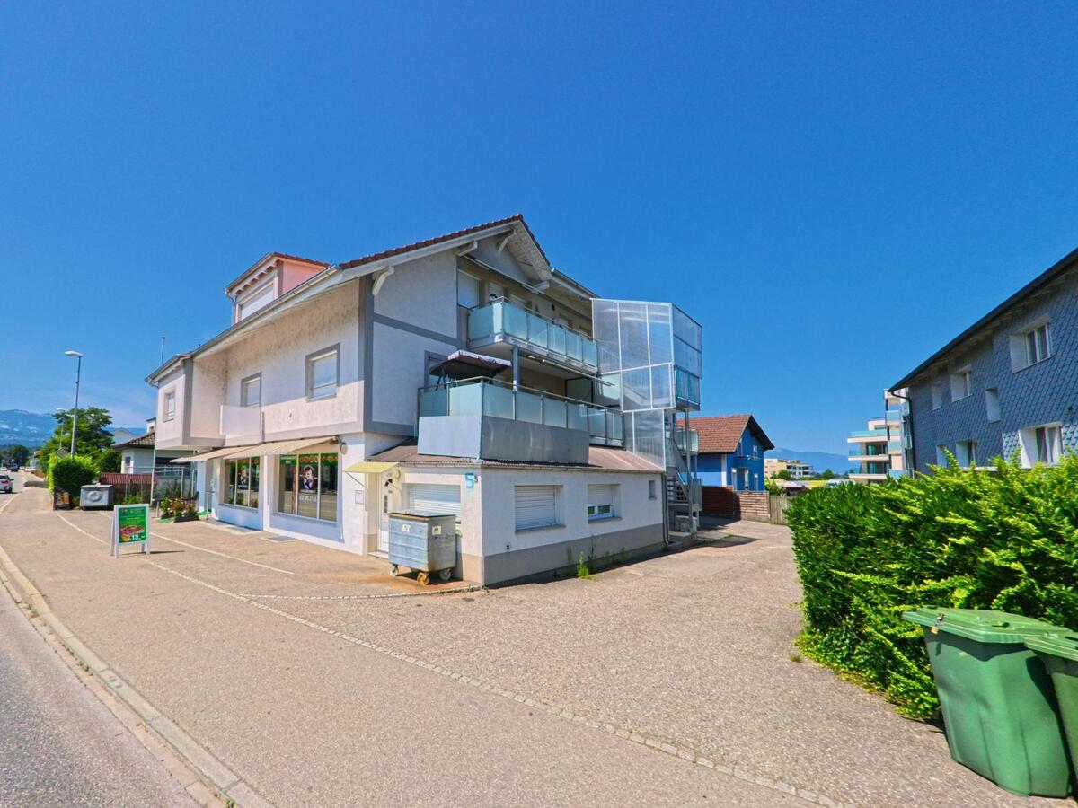 Ein Geschaeftshaus mit Balkonen und Aussentreppe steht in Aegerten (2558, Kanton Bern) an einer Nebenstrasse mit Sicht auf angrenzende Wohnhaeuser.