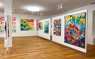 In einer Ausstellung in Bonstetten 8906 im Kanton Zurich werden farbenfrohe Quiltarbeiten und textile Kunstwerke in einem hellen Galerieraum praesentiert.