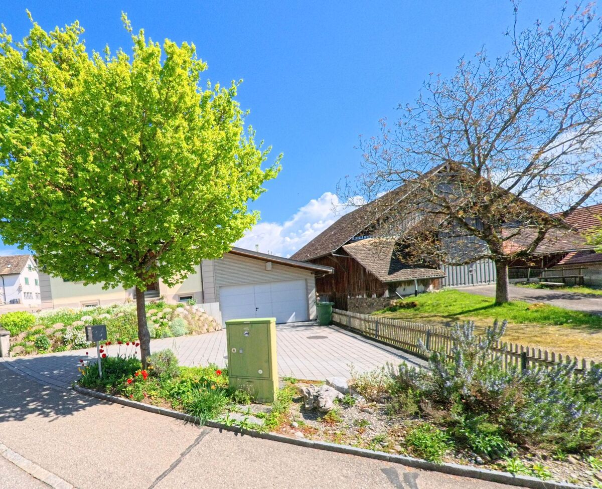 In Aeugst am Albis, PLZ 8914 im Kanton Zürich, steht ein Bauernhaus mit grossem Schindeldach neben einem modernen Garagengebäude, umgeben von gepflegten Gärten und blühenden Tulpen.
