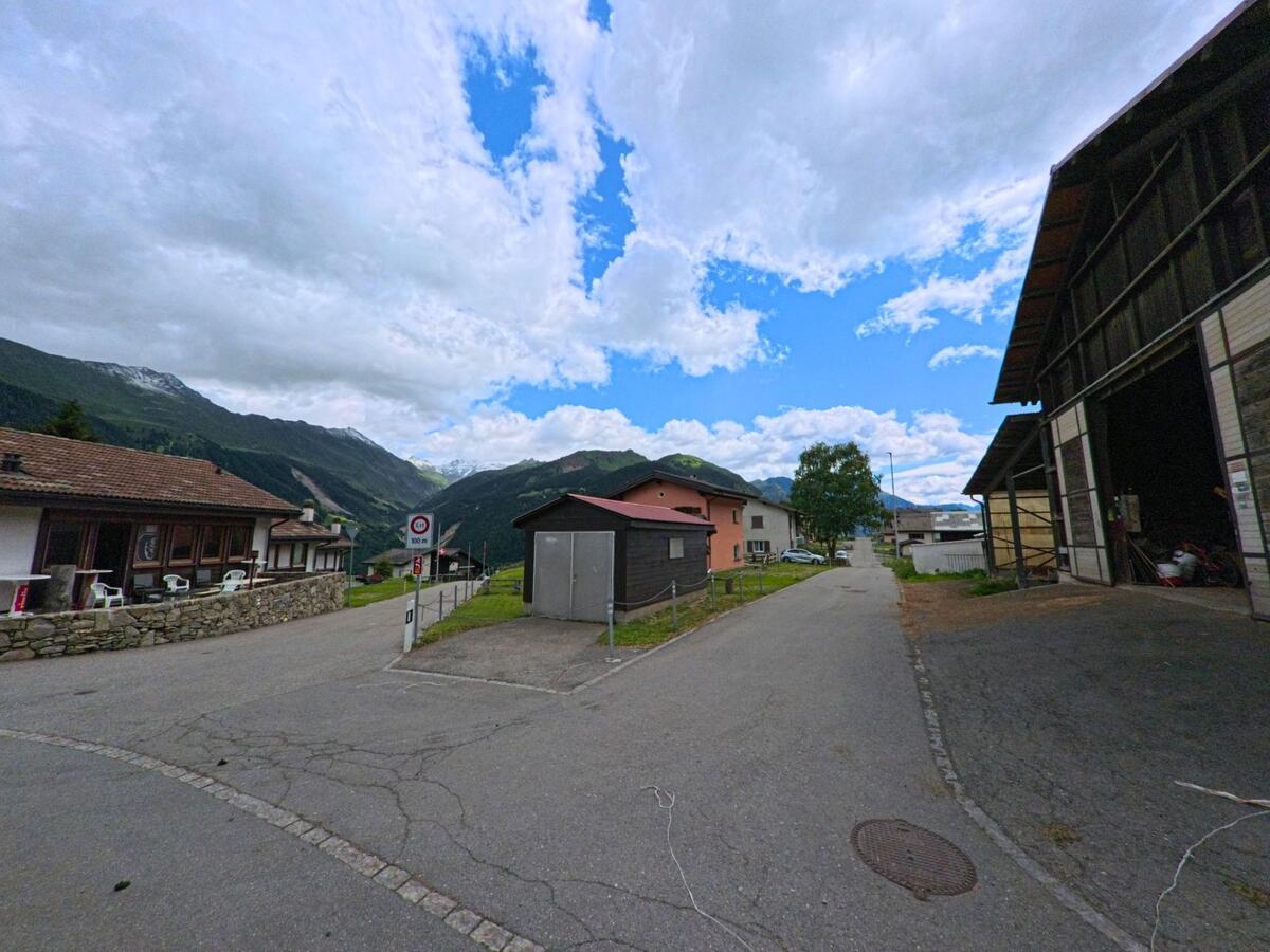 In Airolo (6780, Kanton Tessin) führt eine schmale Strasse durch ein Wohn- und Gewerbegebiet mit Blick auf die umliegenden Alpenhänge.