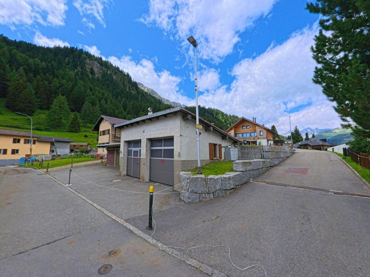Ein kleines Gebäude mit Garagentoren steht in einem ruhigen Wohngebiet von Airolo (6780, Kanton Tessin), umgeben von Chalets und bewaldeten Berghängen.