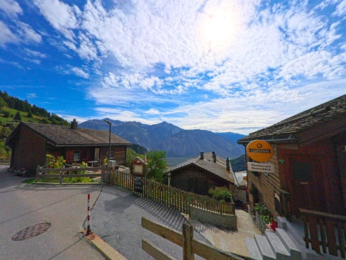 Ein Schild weist zum Restaurant Sunnublick in Albinen (3955, Kanton Wallis), während im Hintergrund die Bergkette unter dem wolkenreichen Himmel erscheint.