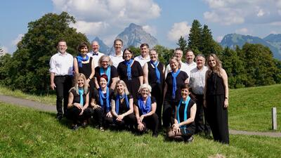 Vor alpiner Kulisse in Arth (6410, Kanton Schwyz) stellt sich der ALLEGRA-Chor Arth auf einer Wiese in zwei Reihen zu einem Gruppenfoto auf.