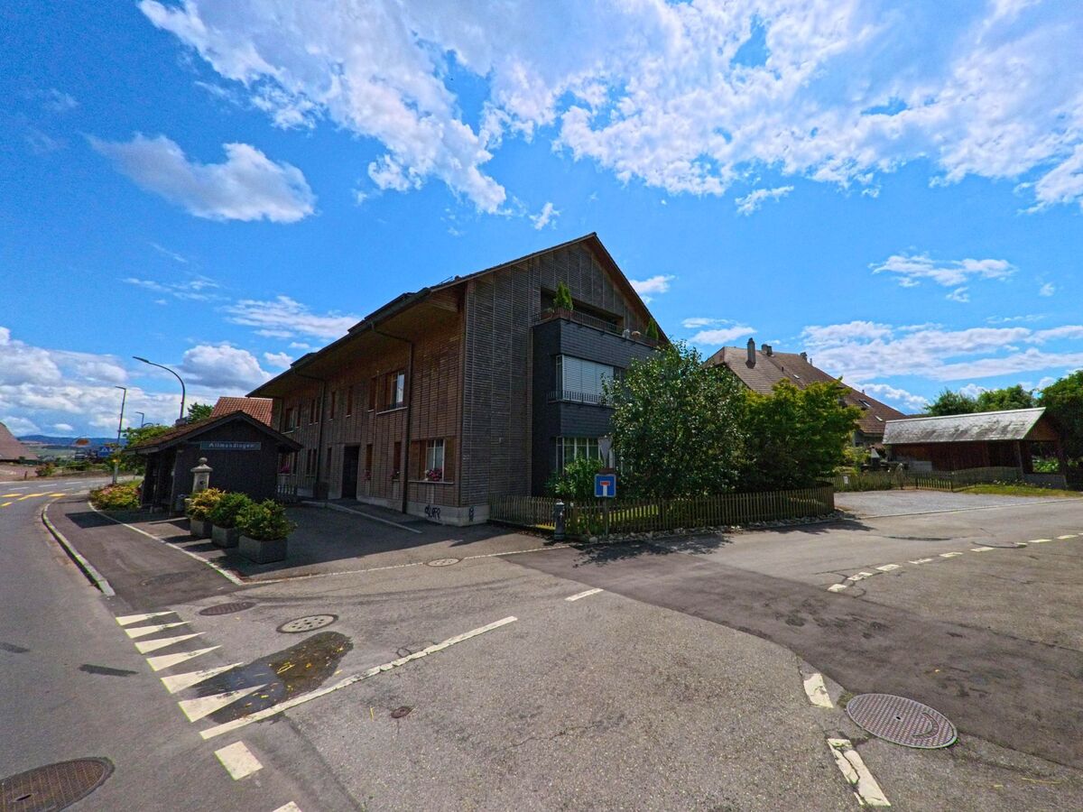An der Allmendstrasse in Allmendingen (3112, Kanton Bern) reihen sich moderne Holzbauten und traditionelle Wohnhäuser entlang einer ruhigen Nebenstrasse mit Sackgassenschild.