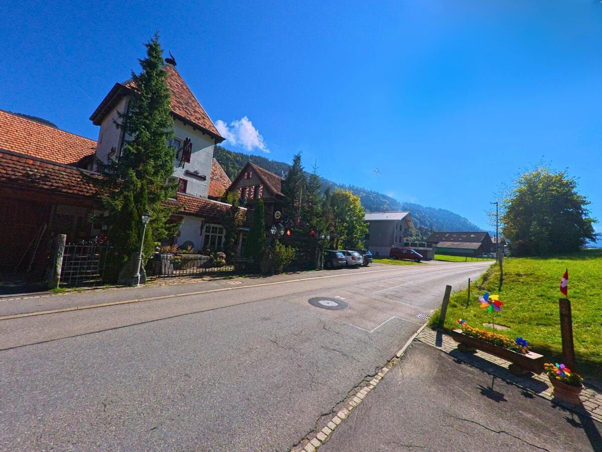 An einer Weggabelung stehen ältere Gebäude im Dorfkern von Alpthal (8849, Kanton Schwyz).