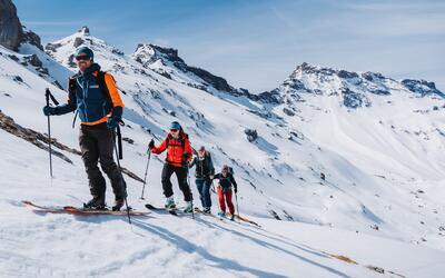 Eine Gruppe der Alpinschule Adelboden Kandersteg aus Adelboden (3715, Kanton Bern) steigt mit Tourenski und Stöcken durch eine verschneite alpine Berglandschaft auf.