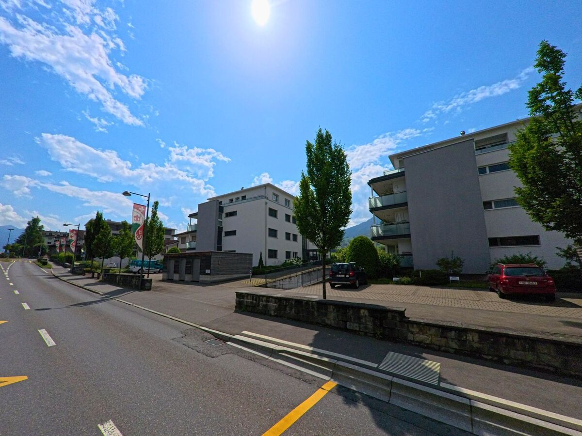 Moderne Wohngebaeude mit Balkonen praegen das Strassenbild in Alpnach (6055, Kanton Obwalden), wo entlang der Fahrbahn Fahnen mit dem Gemeindewappen wehen.