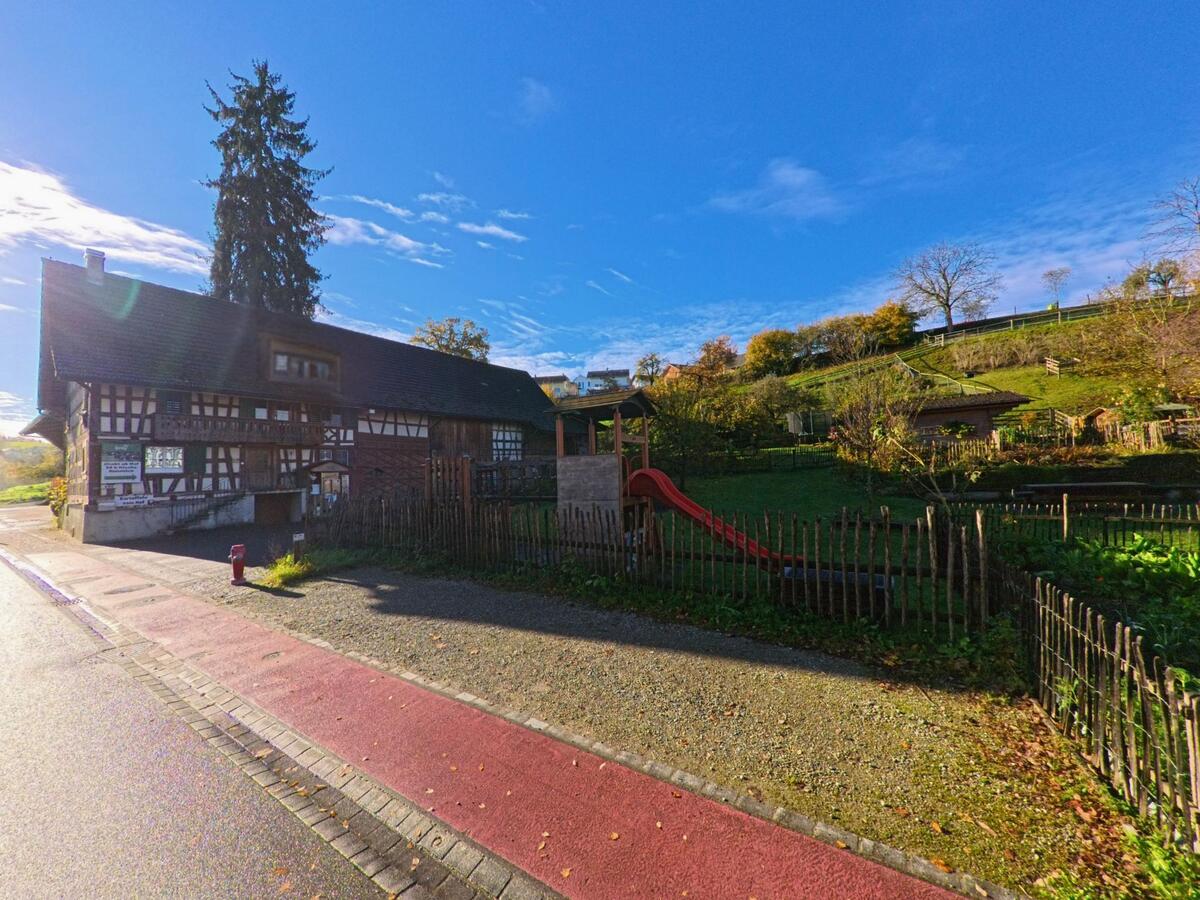 Neben einem historischen Fachwerkhaus mit Gartenanlage erstreckt sich eine Gruenflaeche mit Spielgeraet in Amlikon-Bissegg (8514, Kanton Thurgau) am sonnigen Herbsttag.