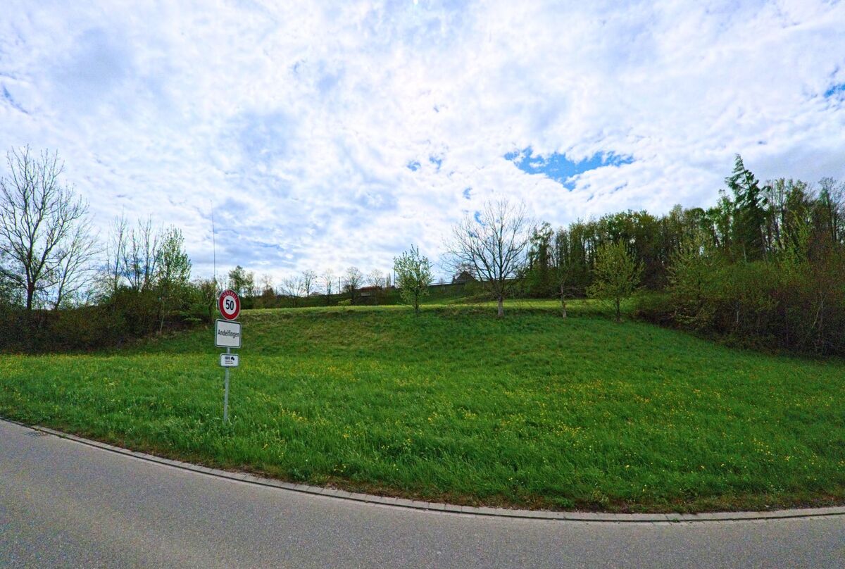  Ein Ortsschild markiert den Beginn von Andelfingen (8453, Kanton Zürich) an einer Landstrasse, die an einer grünen Wiese mit Bäumen vorbeiführt.