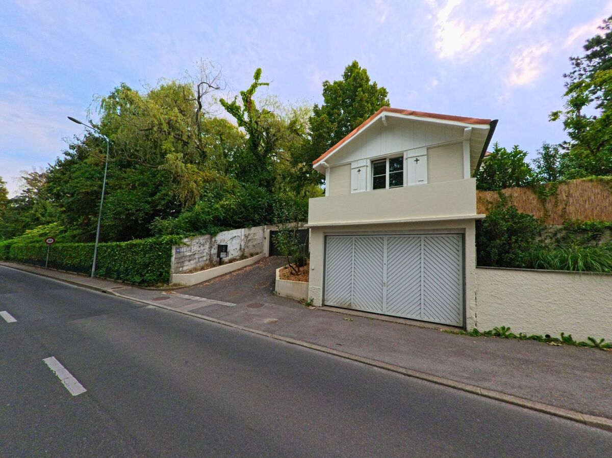 Ein kleines Wohnhaus mit Garagentor steht an einer von Baeumen gesaeumten Strasse in Anieres (1247, Kanton Genf).