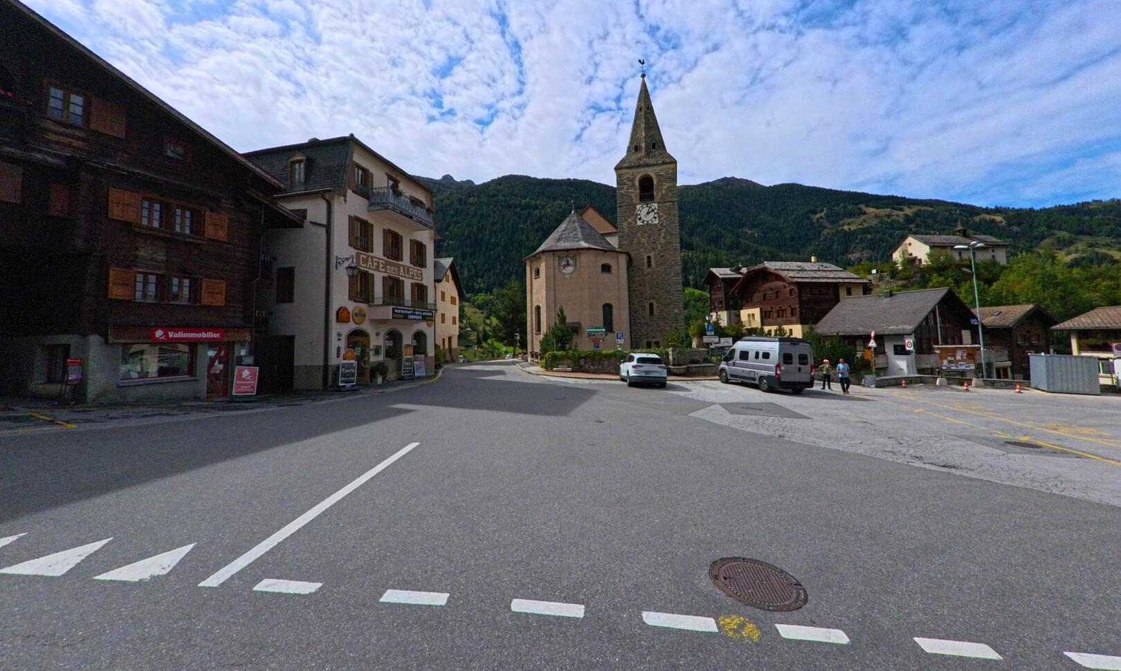 Im Zentrum von Anniviers (3961, Kanton Wallis) steht die Kirche mit ihrem markanten Turm, umgeben von traditionellen Holzhäusern und Bergen im Hintergrund.