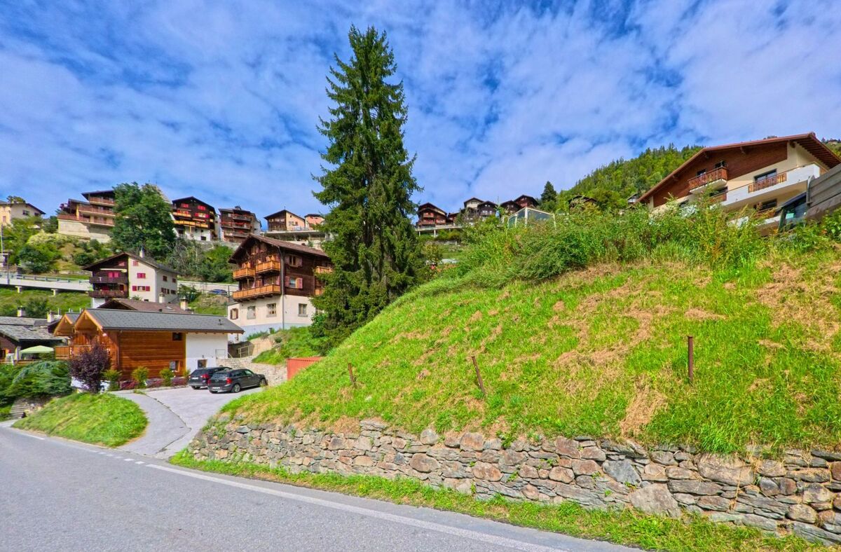 Am Hang von Anniviers (3961, Kanton Wallis) stehen zahlreiche Wohnhaeuser, darunter traditionelle Chalets und moderne Bauten, die sich zwischen Wiesen und Baumen verteilen.