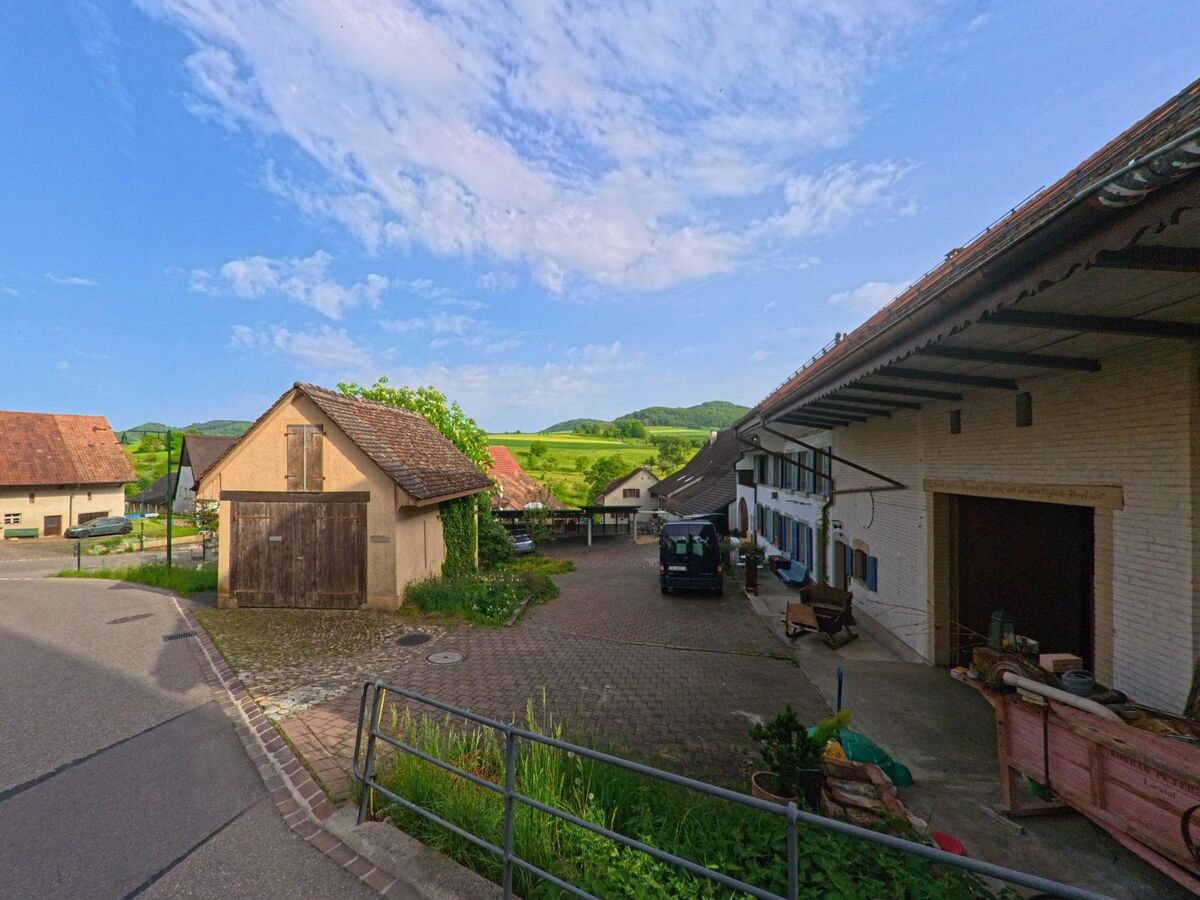 In Anwil (4469, Kanton Basel-Landschaft) öffnet sich ein Blick auf einen Bauernhof mit Nebengebäuden und weitem Ausblick in die grüne Hügellandschaft.