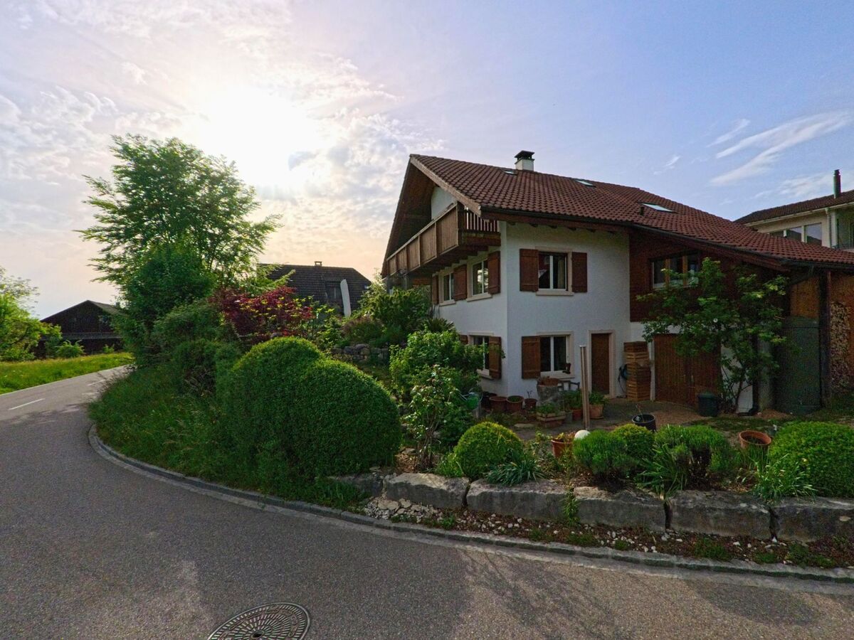 In Anwil (PLZ 4469, Kanton Basel-Landschaft) befindet sich ein Einfamilienhaus mit gepflegtem Vorgarten an einer leicht kurvigen Dorfstrasse bei tiefstehender Sonne.