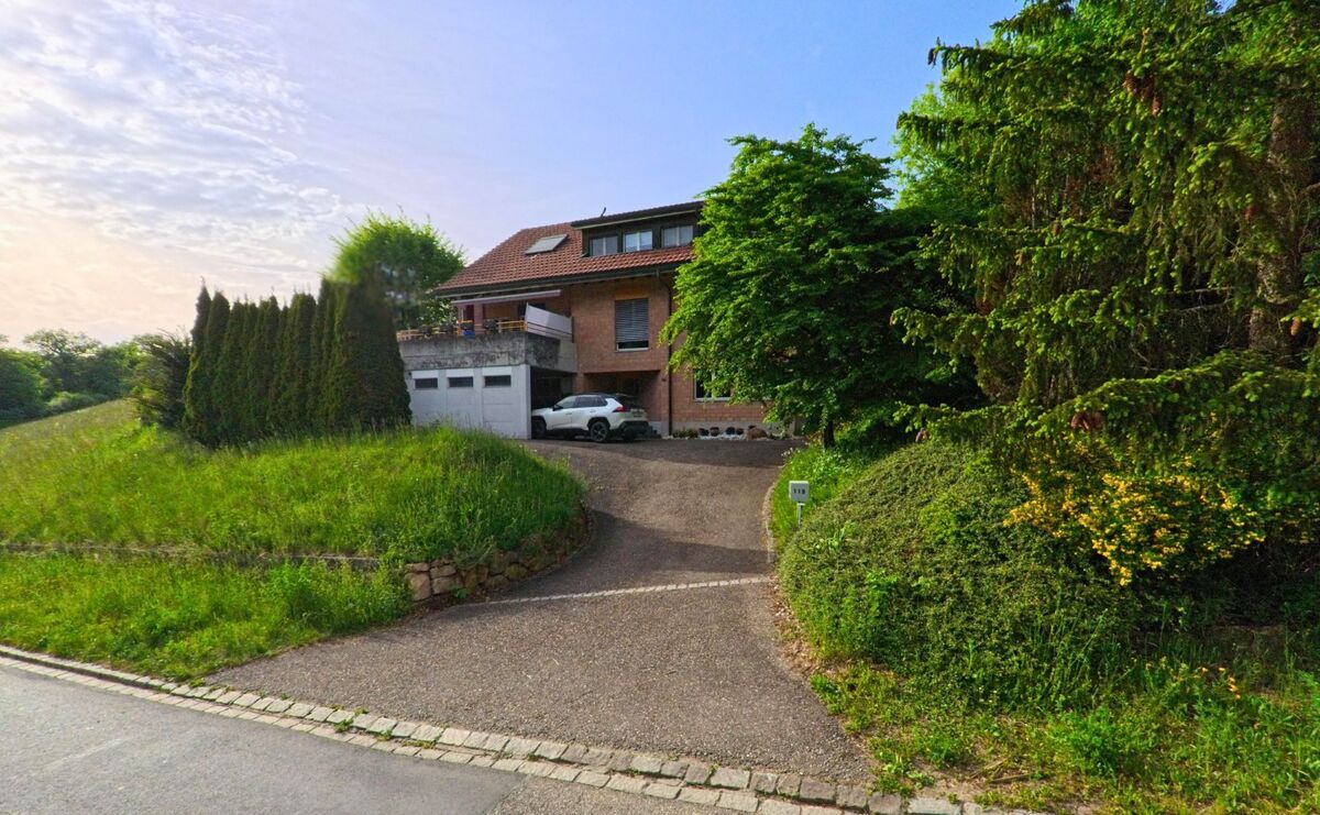 In Anwil (4469, Kanton Basel-Landschaft) liegt ein Einfamilienhaus mit Garage und Zufahrt eingebettet zwischen Bäumen und dichtem Grün.