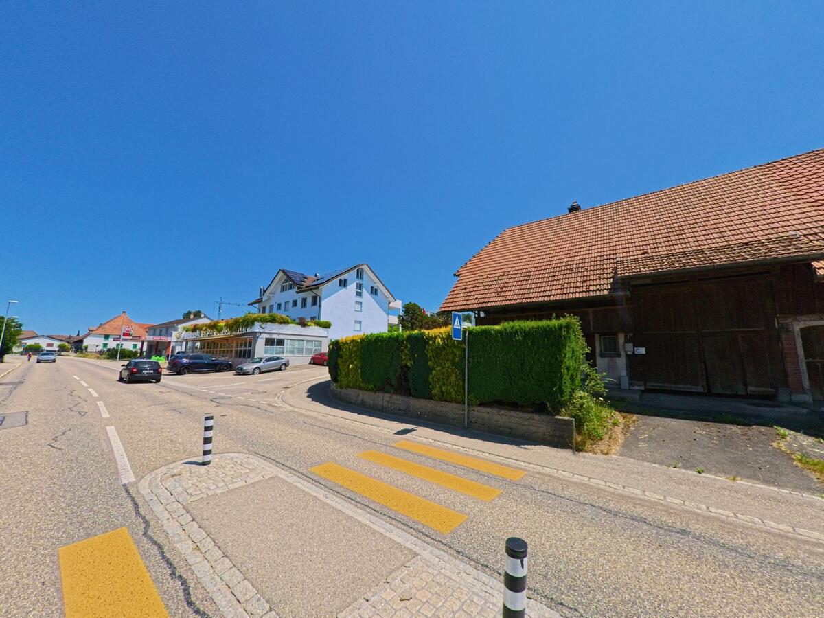 In Arch (3296, Kanton Bern) treffen moderne und traditionelle Architektur an einer verkehrsberuhigten Strasse mit Zebrastreifen und Parkplätzen aufeinander.