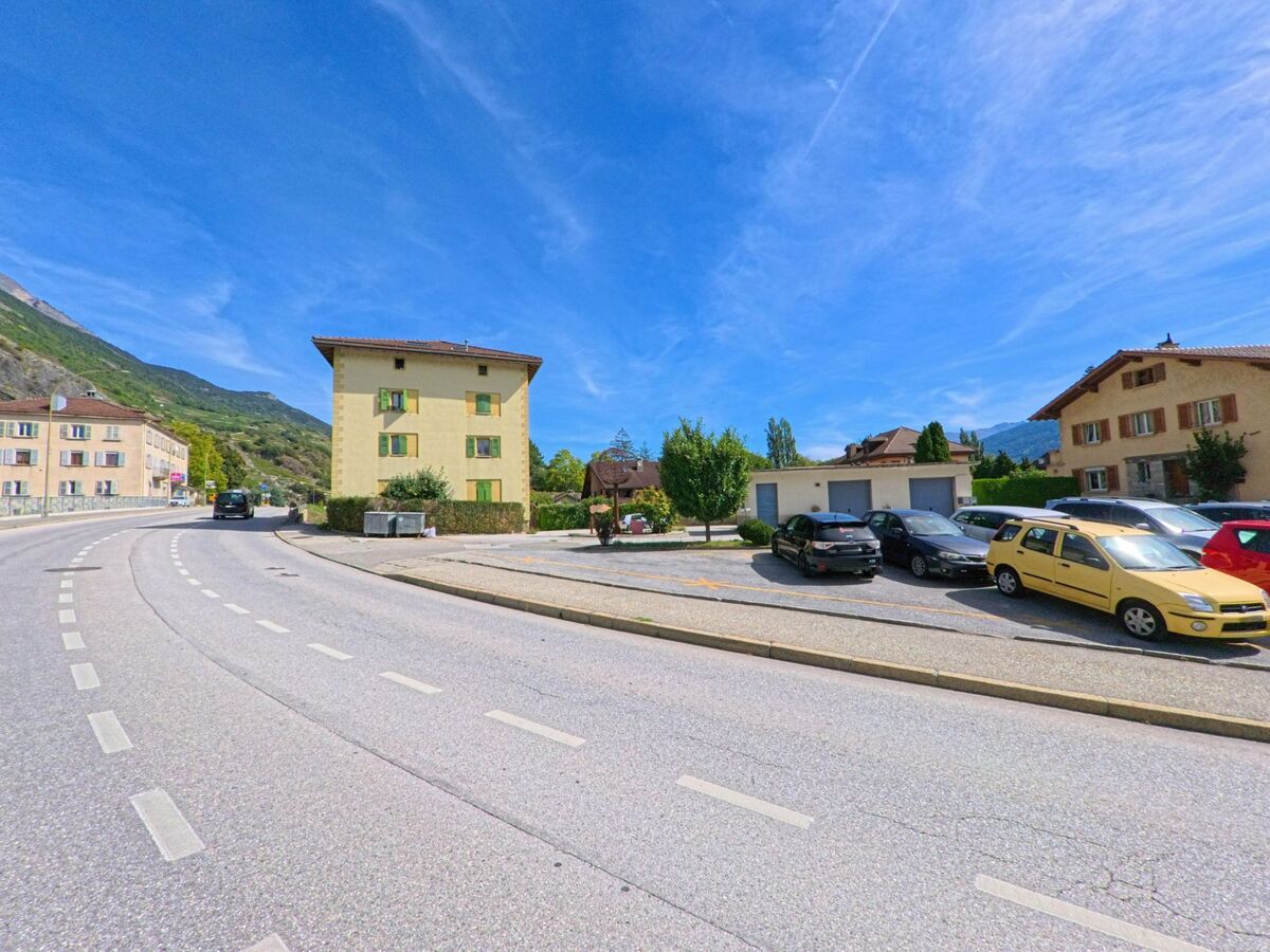 Mehrfamilienhaeuser mit gruener Fensterlaeden praegen in Ardon (1957, Kanton Wallis) das Ortsbild entlang einer leicht gekruemmten Strasse.