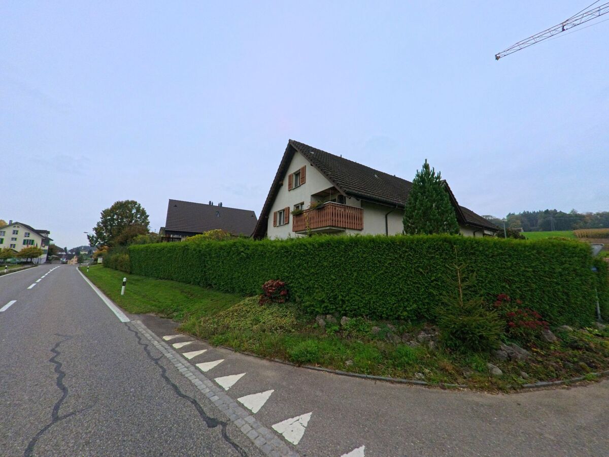 Ein Wohnhaus mit Holzbalkon und dichter Hecke steht in Aristau (5628, Kanton Aargau) entlang einer ruhig verlaufenden Strasse.