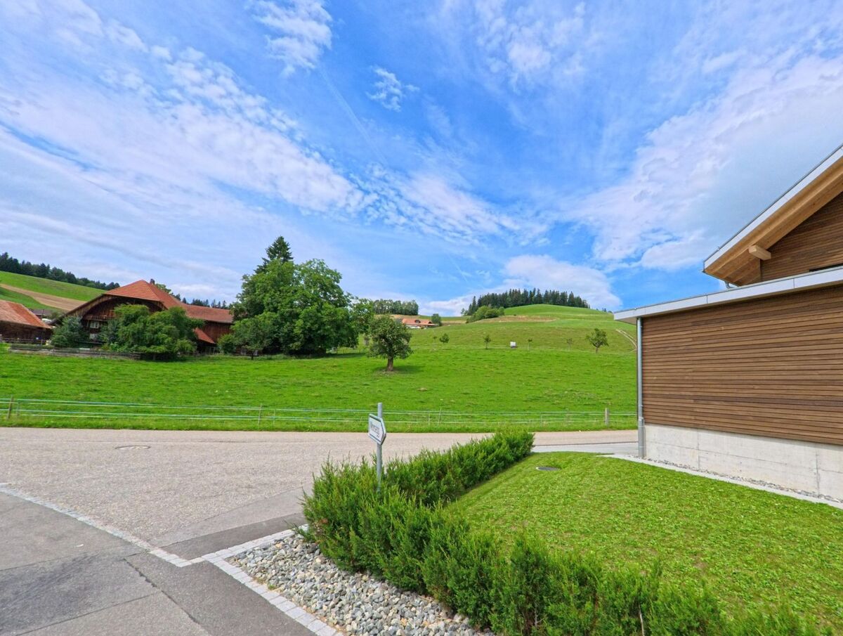 Am Ortsrand von Arni (3508, Kanton Bern) öffnet sich der Blick von einem modernen Gebäude aus auf grüne Weiden, einzelne Bäume und traditionelle Bauernhöfe.