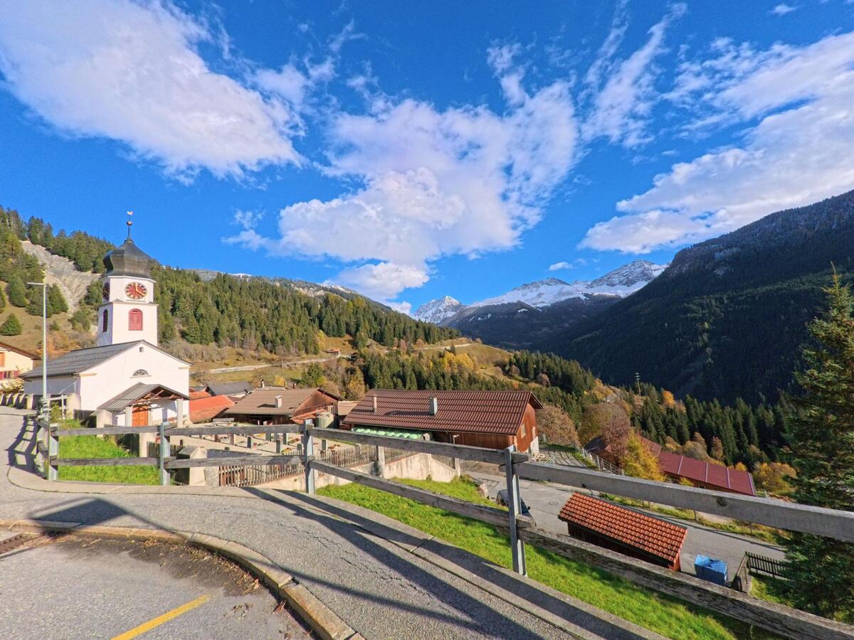 Mit Blick über Dächer und Hanglagen zeigt sich in Arosa (7029, Kanton Graubünden) ein Kirchengebäude oberhalb des Tals vor bewaldeten Berghängen.