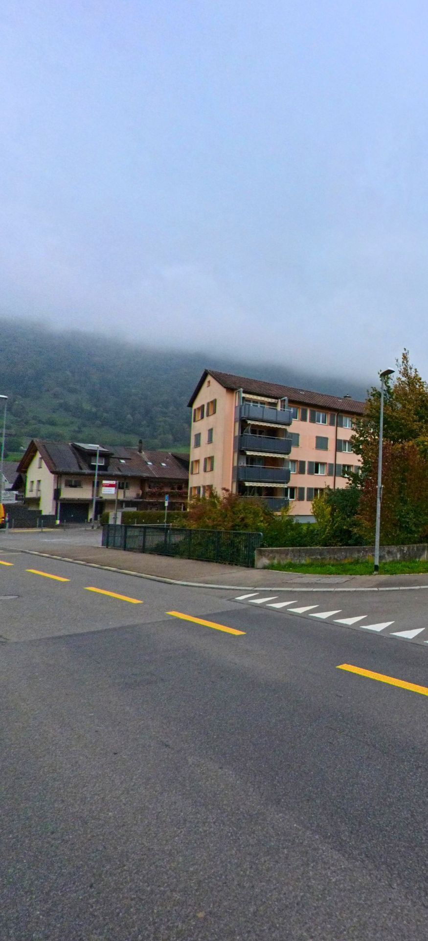 Vor den nebelverhangenen Haengen von Arth (6415, Kanton Schwyz) steht ein mehrstockiges Wohnhaus mit Balkonen an einer verkehrsarmen Strasse.