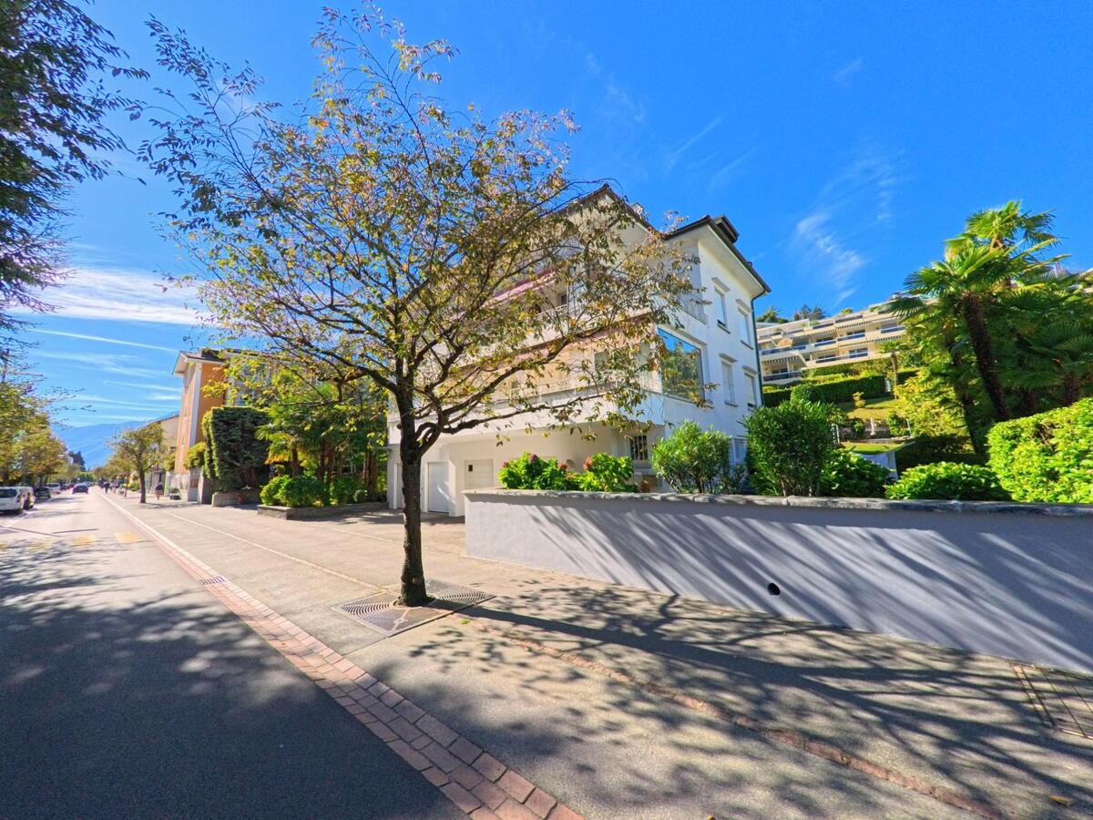 In Ascona (6612, Kanton Tessin) steht ein helles Wohnhaus an einer ruhigen, von Bäumen gesäumten Strasse mit Blick auf terrassierte Hänge.