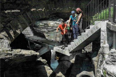 In Li Curt (7745, Kanton Graubünden) steht eine Besuchergruppe auf einer Brücke über schroffe Felsen und Bäche im Giardino dei Ghiacciai, dem Cavaglia Glacier Garden.