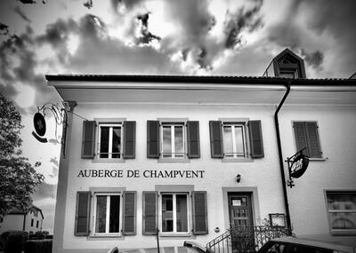 Das Restaurant Auberge de Champvent in Champvent (1443, Kanton Waadt) zeigt seine Fassade mit Fensterläden unter einem dramatisch bewölkten Himmel.