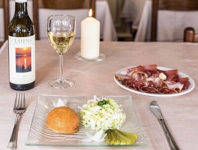 In der Auberge de Luins in Luins (1184, Kanton Waadt) steht auf einem gedeckten Tisch ein Glas Weisswein, eine Flasche Luins 2015, ein Gericht mit Fleisch und Salat sowie eine brennende Kerze.