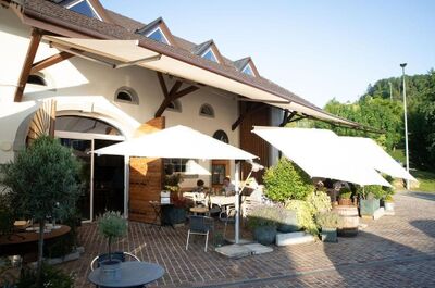 Vor einem Restaurant in Zeihen (5079, Kanton Aargau) stehen unter grossen Sonnenschirmen Tische und Stuehle auf einem gepflasterten Platz.