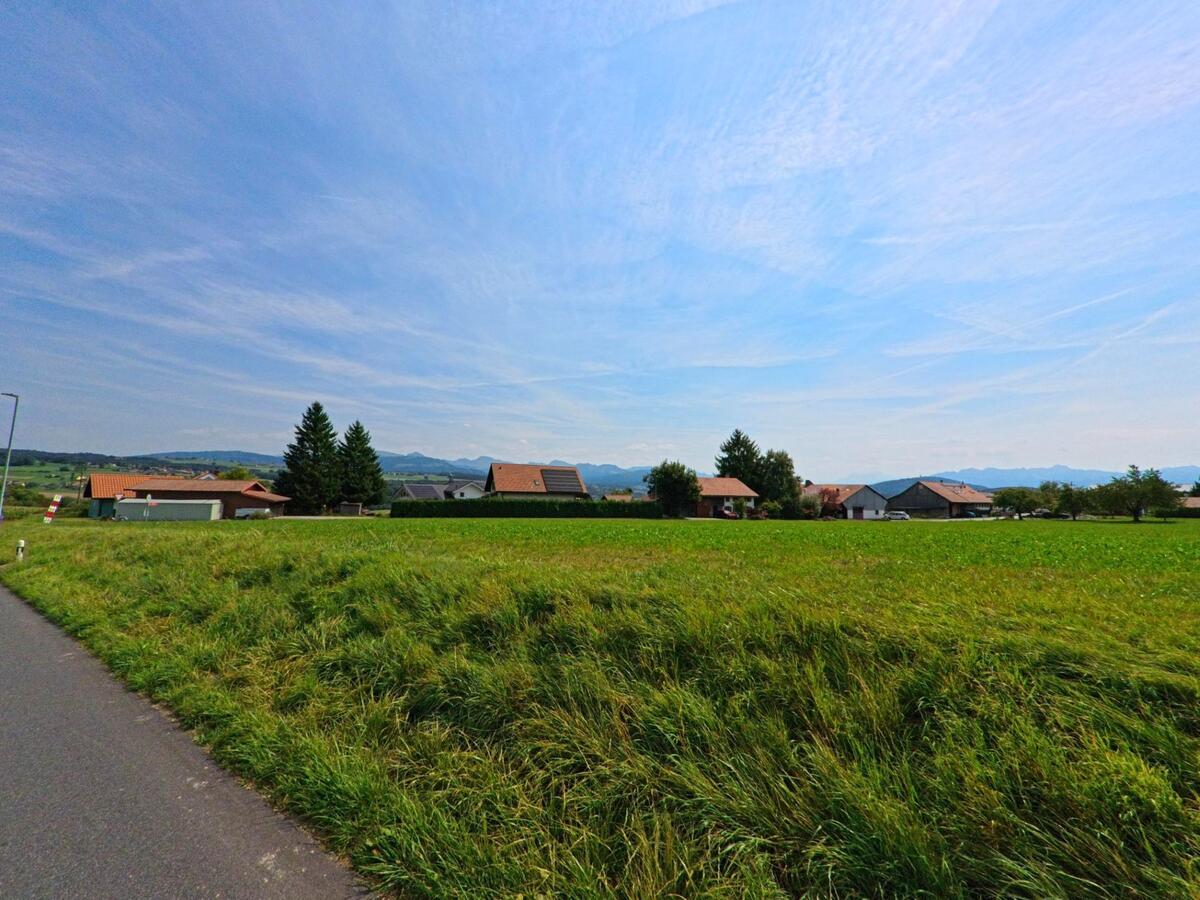Über eine weite Wiesenfläche hinweg zeigt sich der Dorfrand von Auboranges (1673, Kanton Freiburg) mit einzelnen Wohnhäusern vor einer sanften Hügellandschaft.