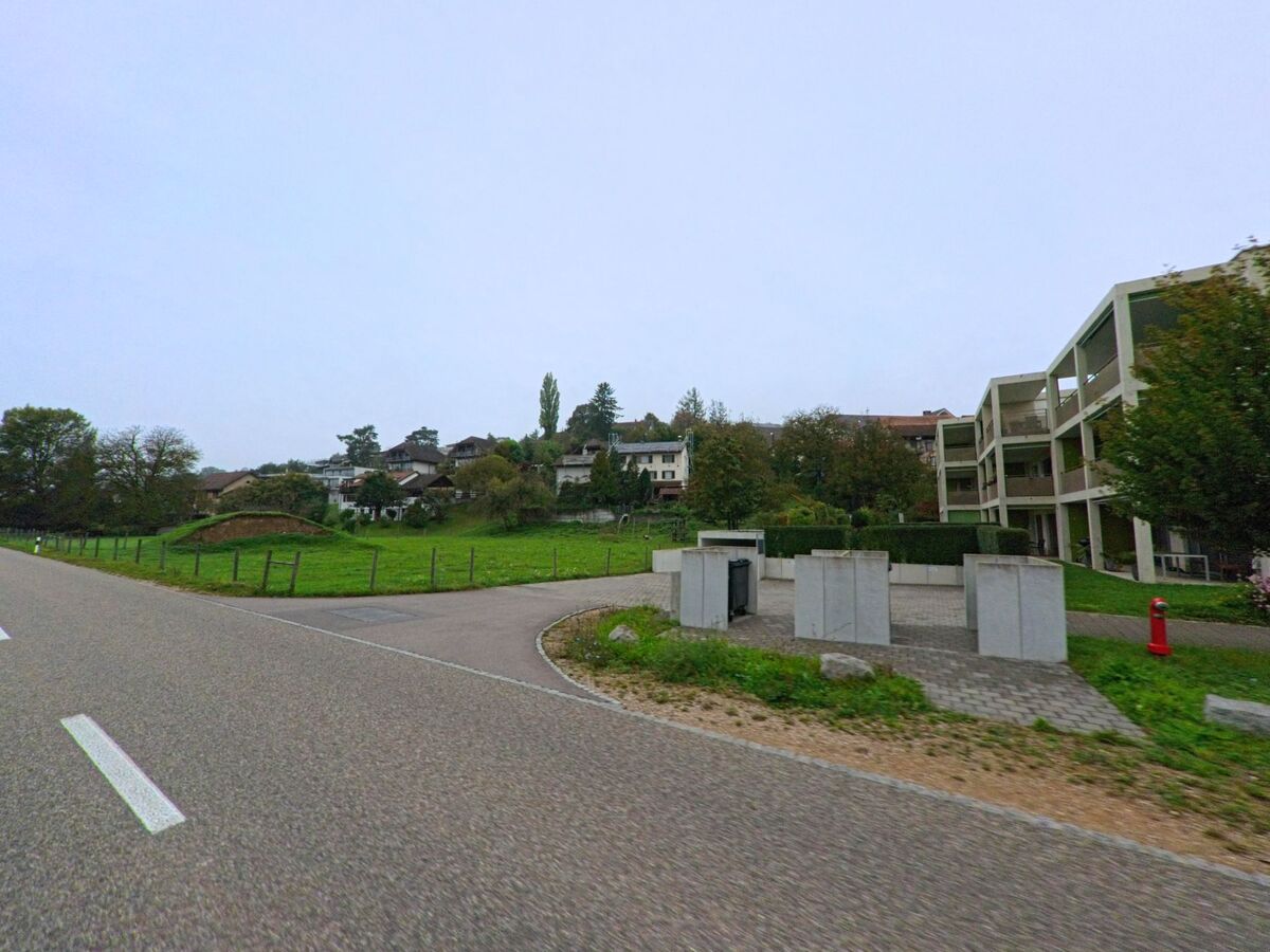 An der Hauptstrasse in Auenstein (5105, Kanton Aargau) liegen moderne Mehrfamilienhäuser neben einer grünen Wiese mit Blick auf den Dorfhang.