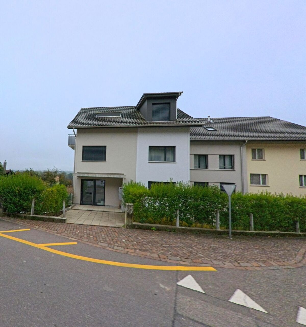Ein modernes Mehrfamilienhaus mit heller Fassade und gepflegtem Vorplatz steht an einer Strassenkreuzung in Auenstein (5105, Kanton Aargau).