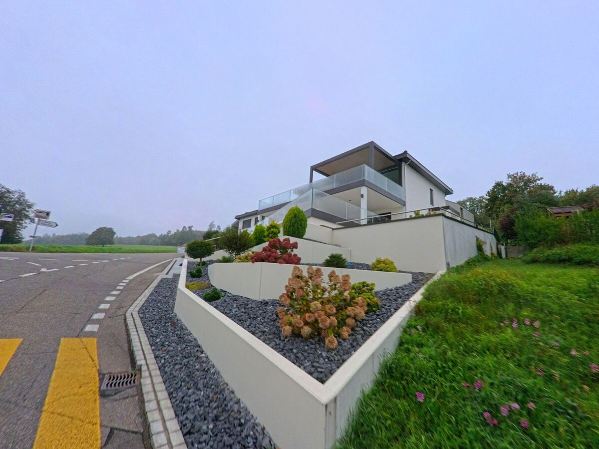 Ein modernes Einfamilienhaus mit klaren Linien und gepflegter Terrassengestaltung steht an einer Strassenkurve in Auenstein (5105, Kanton Aargau).